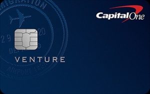 Capital One Venture Rewards credit card shown on a dark blue background, featuring a silver chip on the left, the word ‘Venture’ below it, a subtle airplane and travel-themed pattern in the background, and the Capital One logo in the top-right corner, conveying a premium travel rewards credit card design.